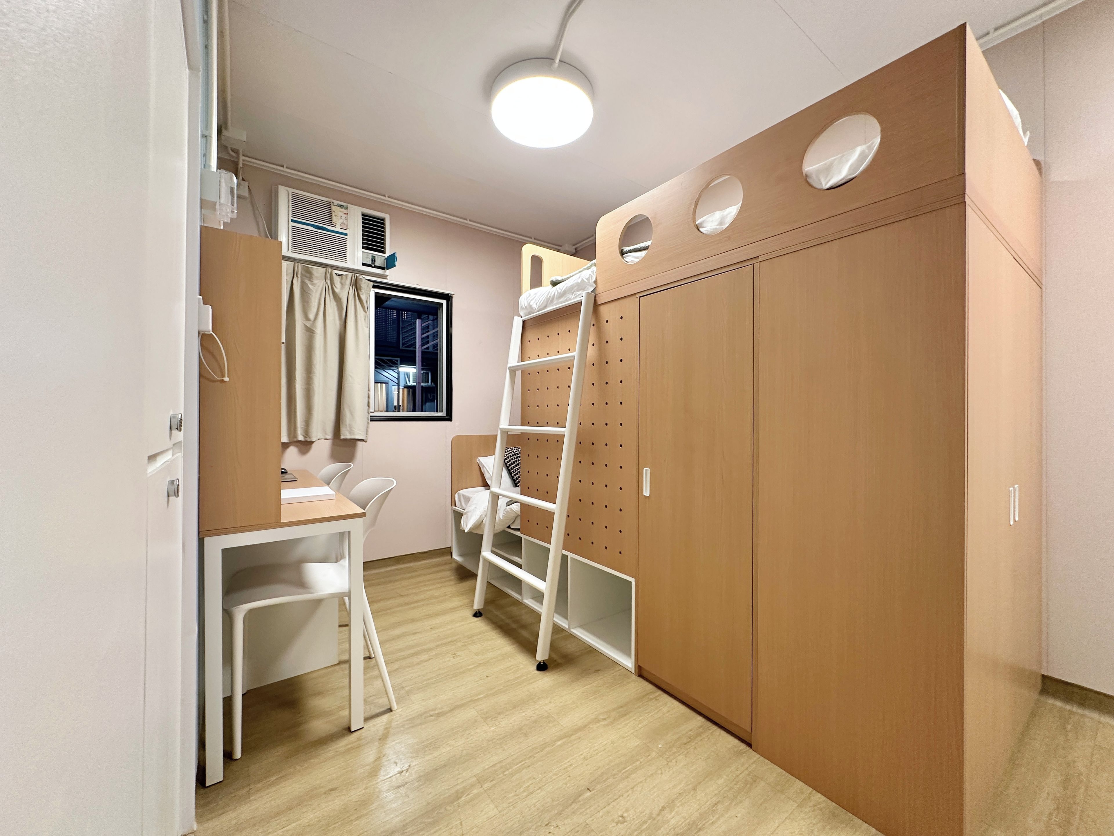 Una habitación con un armario de madera, un escritorio blanco con silla y una ventana con cortinas.
