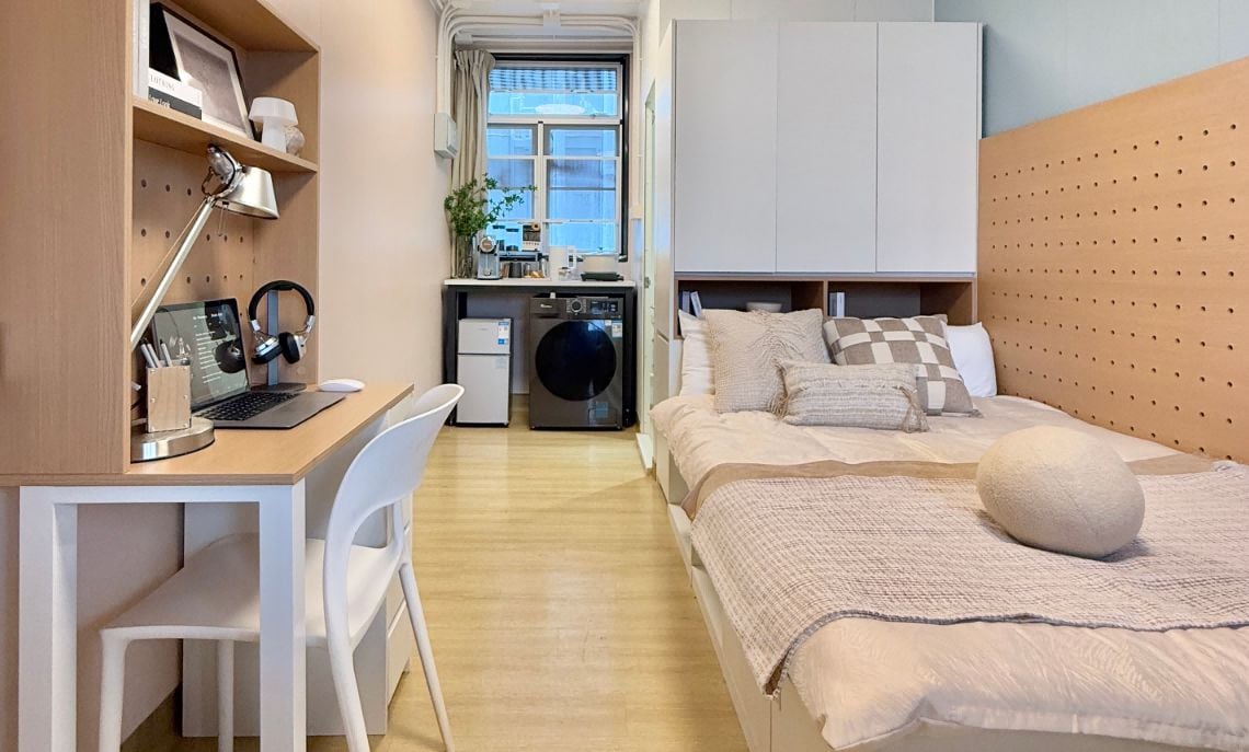 Ett litet rum med en säng, ett skrivbord och en tvättmaskin.
