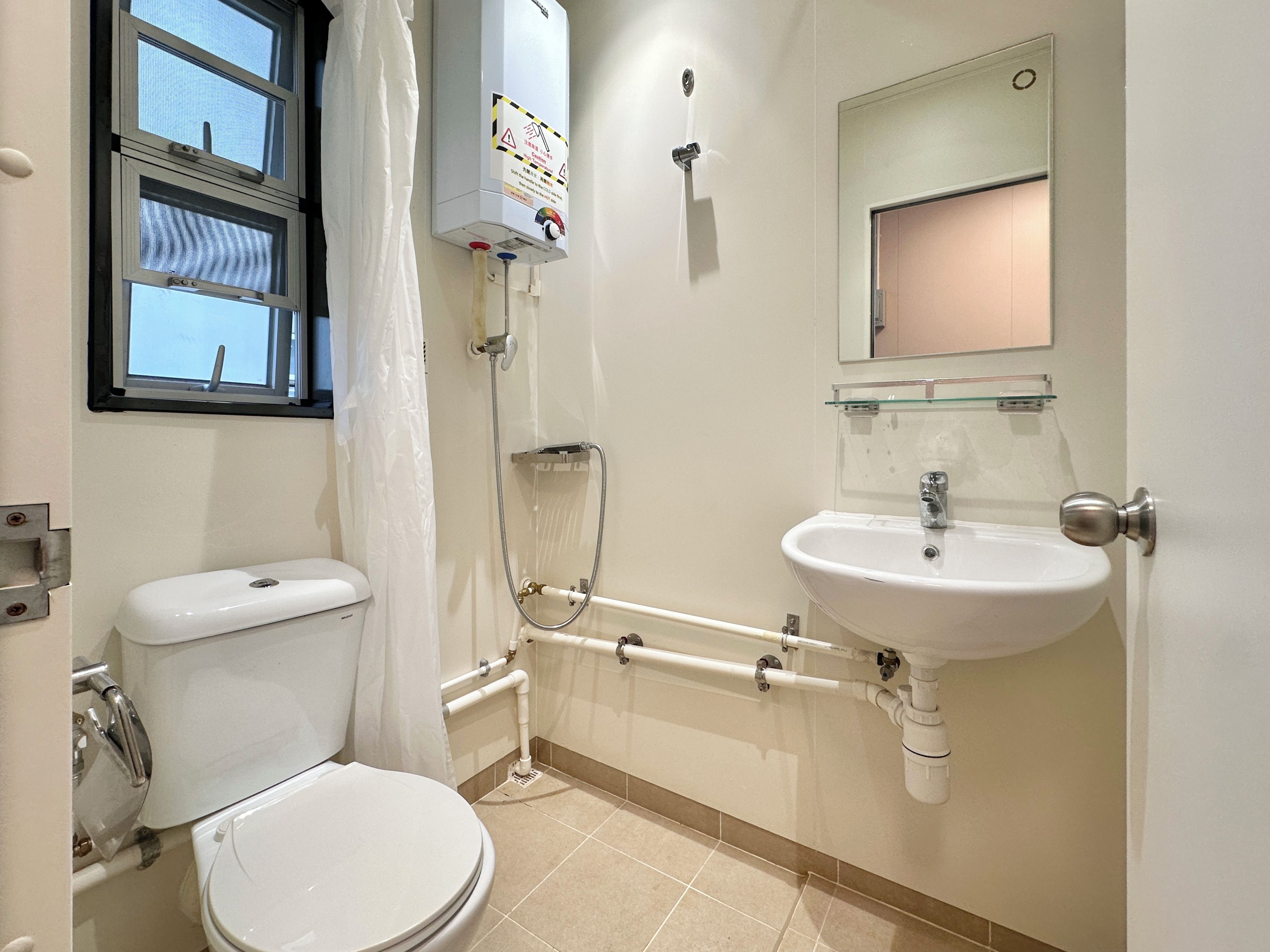Et badeværelse med toilet, bruser, vask og et vindue.