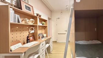 A compact room with a bunk bed, a desk with a chair, a pegboard wall with various items, and a door leading to another room.