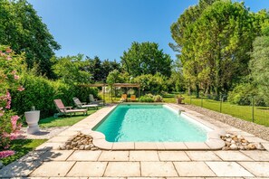 A rectangular swimming pool with a stone border, surrounded by a stone patio, and a pergola with chairs. - Guest Room “Chambre Lilas” with Shared Pool, Wi-Fi and Air Conditioning (Pernes-les-Fontaines)