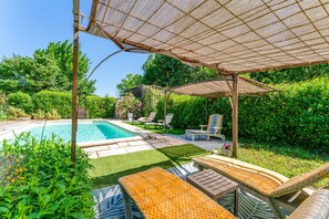 Un área de piscina con sillas de descanso, una pérgola y un césped bien cuidado.