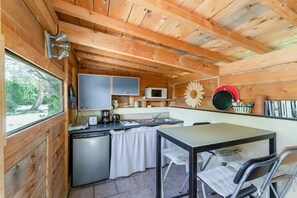 A compact kitchen with a refrigerator, microwave, and sink, wooden walls, and a dining area with a table and chairs. - Sauge Room with Shared Pool, Wi-Fi, and Air Conditioning (Pernes-les-Fontaines)