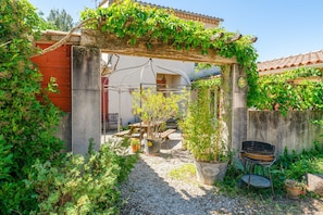A garden with a pergola, potted plants, a barbecue grill, and a gravel path. - Sauge Room with Shared Pool, Wi-Fi, and Air Conditioning (Pernes-les-Fontaines)