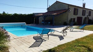 Ein Swimmingpool mit Liegestühlen, eine überdachte Terrasse und ein Gebäude mit einem Ziegeldach.