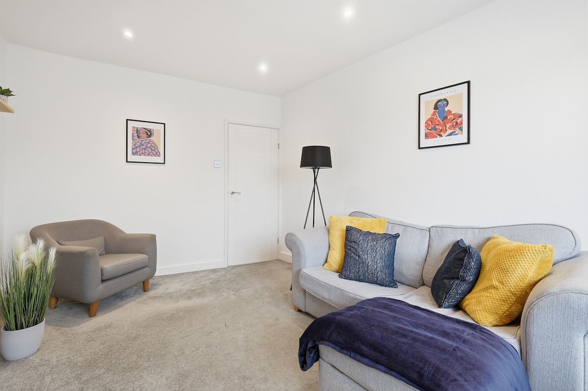 Un salon avec un canapé gris, un fauteuil plus petit, une lampe sur pied et deux œuvres d’art encadrées accrochées aux murs.