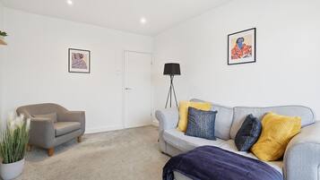 Un salon avec un canapé gris, un fauteuil plus petit, une lampe sur pied et deux œuvres d’art encadrées accrochées aux murs.
