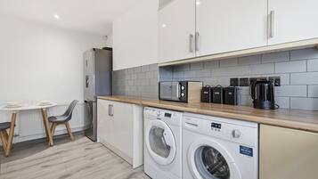 A compact kitchen with a washing machine, a coffee maker, and a microwave.