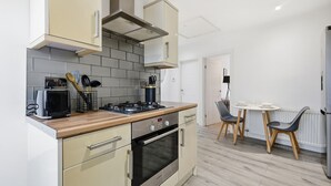 Eine kompakte Küche mit Herd, Backofen und Mikrowelle, ein Essbereich mit Tisch und Stühlen sowie eine weiße Tür im Hintergrund.