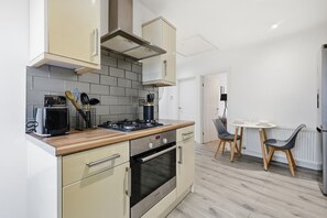 Une cuisine compacte équipée d’une cuisinière, d’un four et d’un four à micro-ondes, un coin repas avec une table et des chaises, et une porte blanche en arrière-plan.