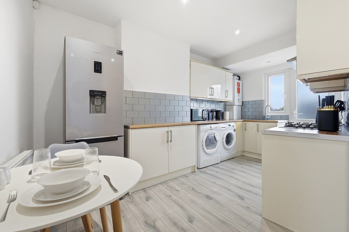 A modern kitchen with a built-in washing machine, a refrigerator, and a dining area with a table set for two.