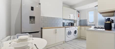A modern kitchen with a built-in washing machine, a refrigerator, and a dining area with a table set for two.