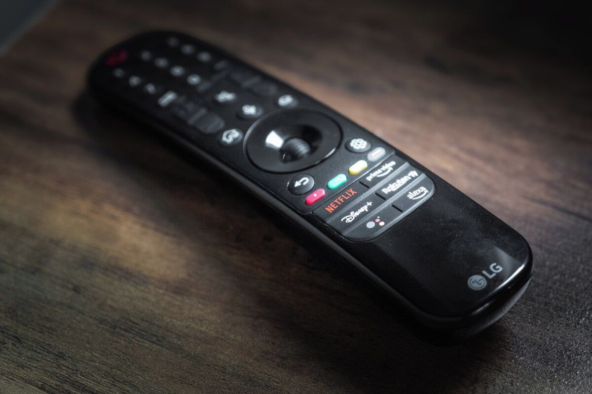 Eine schwarze Fernbedienung mit Tasten für Netflix, Disney+ und weitere Funktionen, auf einer Holzoberfläche platziert.