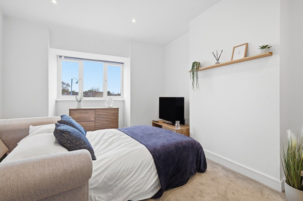 Een slaapkamer met een bed, een televisie, een raam en een plank met planten.