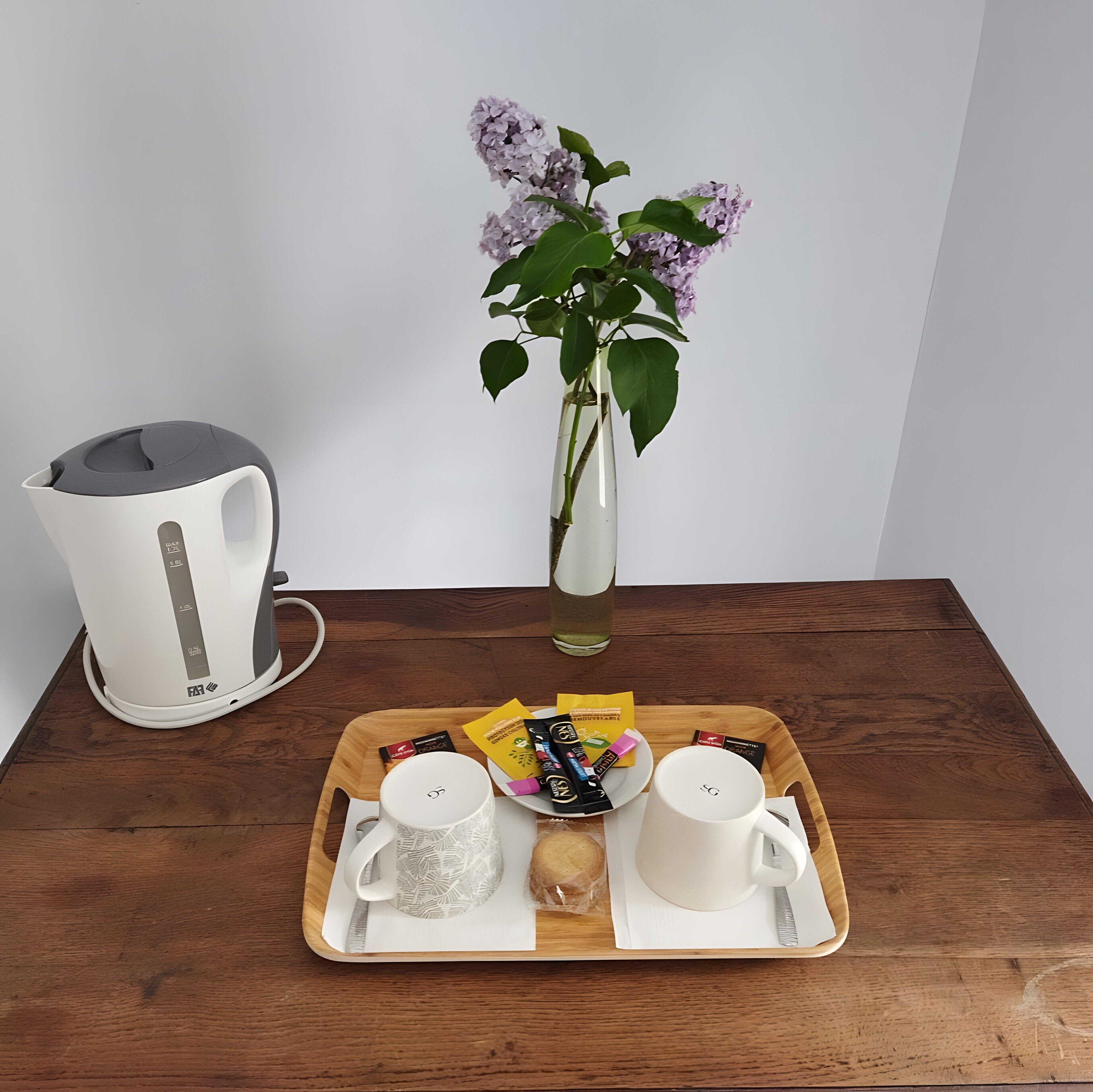 Un plateau en bois sur lequel se trouvent une tasse blanche, une tasse à motifs et un biscuit, le tout posé sur une table en bois.