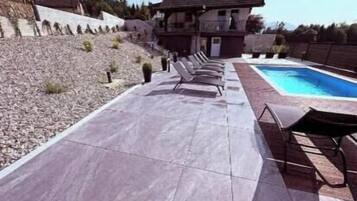 Un espace aménagé au bord de la piscine, avec des chaises longues, une piscine et une maison en arrière-plan.