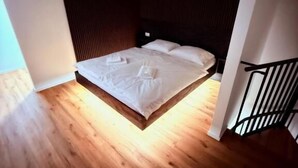 Un dormitorio con piso de madera, una cama con ropa blanca y un cabecero oscuro.