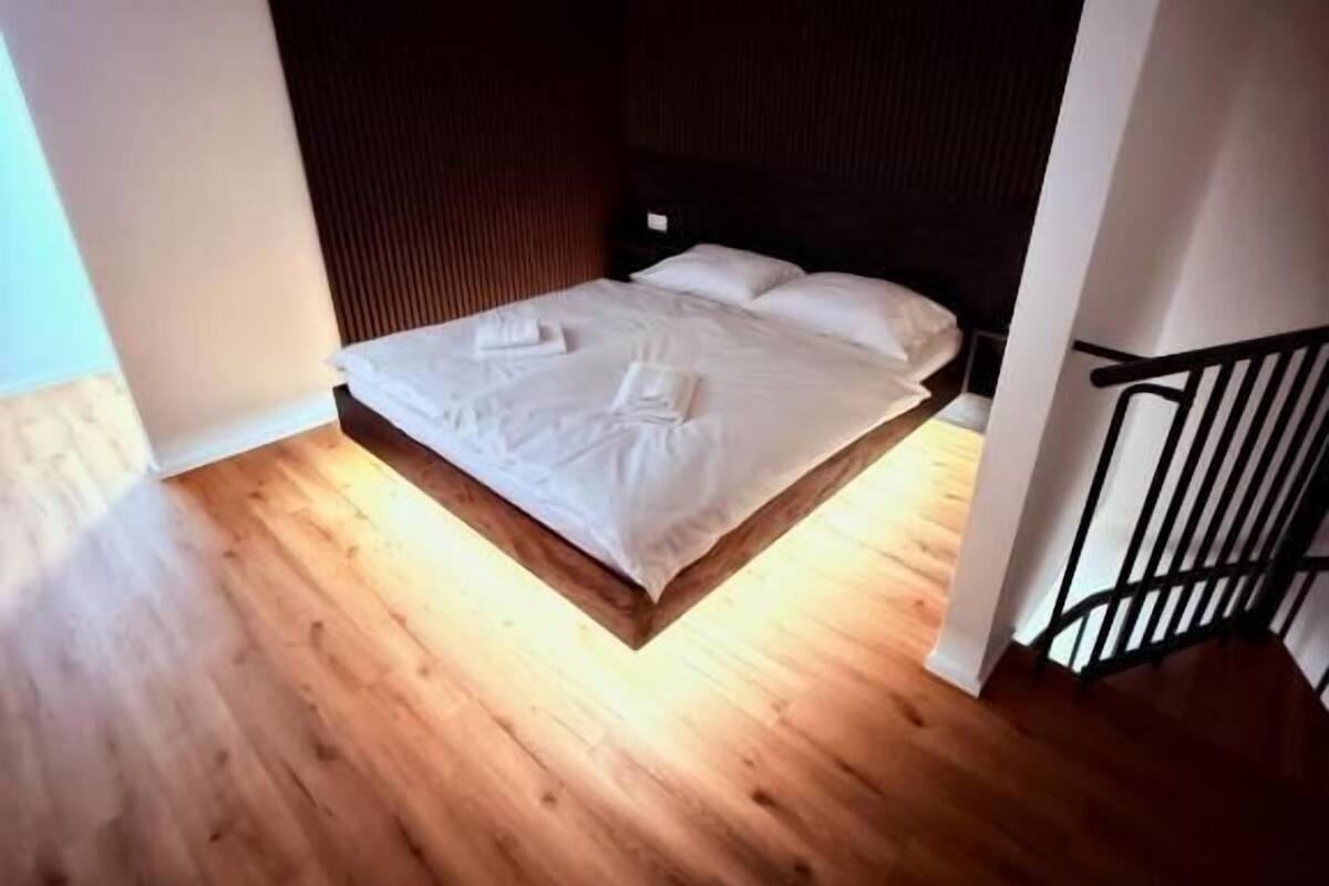 Ein Schlafzimmer mit Holzboden, einem Bett mit weißen Leinen und einem dunklen Kopfteil.