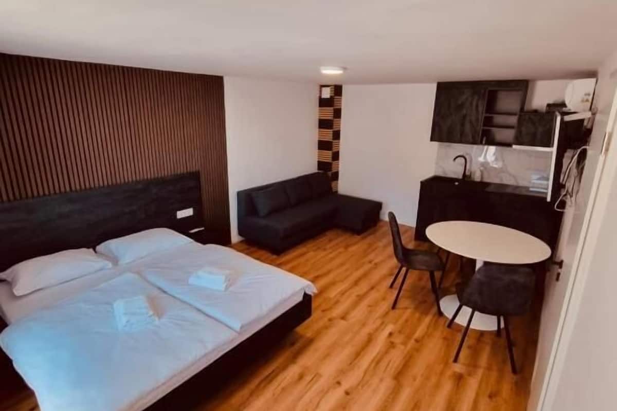 Ein Schlafzimmer mit Bett, einer Couch, einem Esstisch mit Stühlen und einer Küchenzeile.