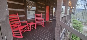 Une véranda en bois avec des fauteuils à bascule et une porte rouge.