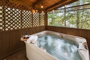 Ein hölzerner Wellnessbereich mit Whirlpool, Holzlattenwänden und Blick auf Bäume.