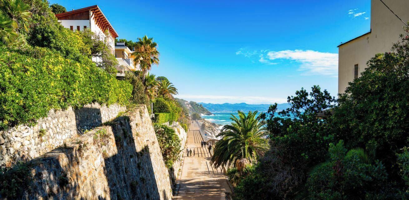 A coastal road with stone walls, a staircase, and buildings with red roofs.