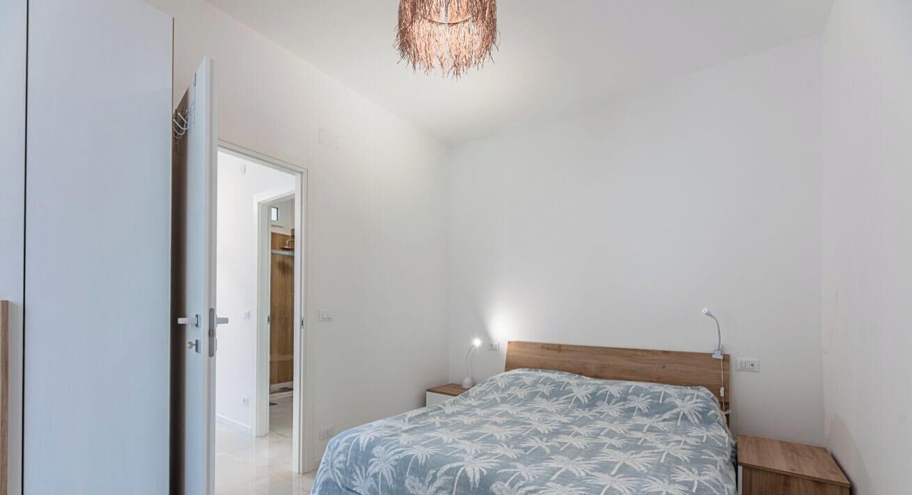 A bedroom with a bed, bedside table, and a hanging light fixture.