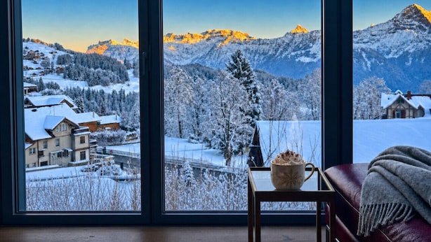 A room with a large window offering a view of a snowy mountain landscape. - Concierge, Lake Thun/Alps Scenic Views by SwissHut (Beatenberg)