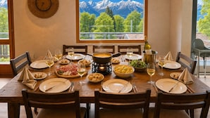 A dining table set for a meal with a mountain view, a clock on the wall, and a bottle of wine. - Concierge, Lake Thun/Alps Scenic Views by SwissHut (Beatenberg)