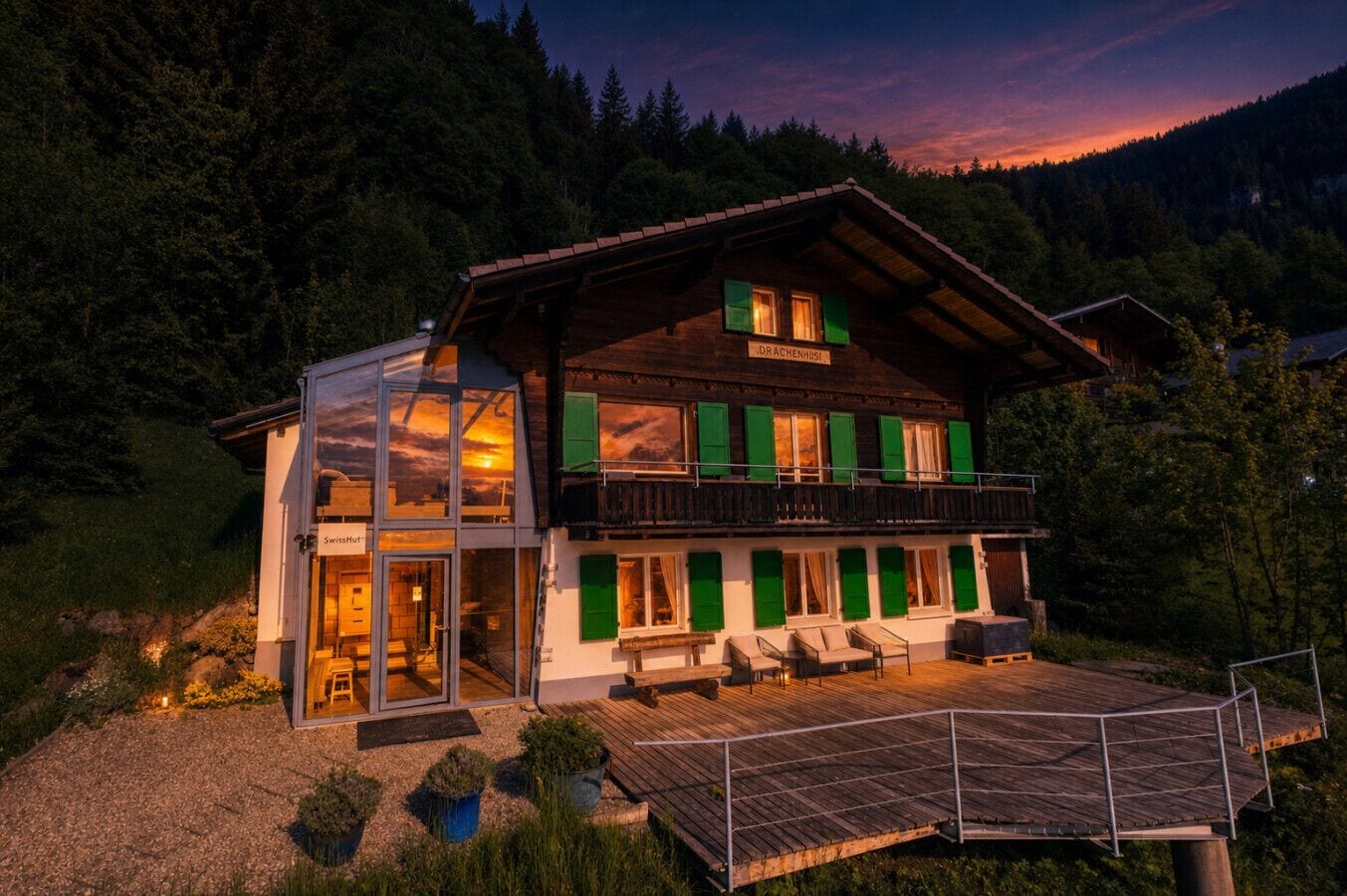 A two-story chalet with a balcony, a glass entrance, and a wooden deck.