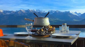 A table set with a pot, glasses, and a bottle, overlooking a mountain range. - Concierge, Lake Thun/Alps Scenic Views by SwissHut (Beatenberg)