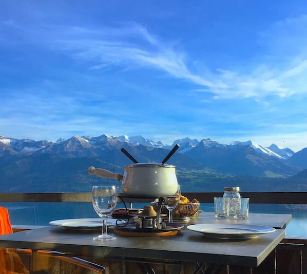 Une table dressée avec une théière, des verres et une bouteille, donnant sur une chaîne de montagnes.