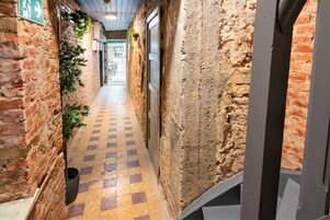 Un pasillo estrecho con paredes de ladrillo, piso a cuadros y una puerta a la derecha.