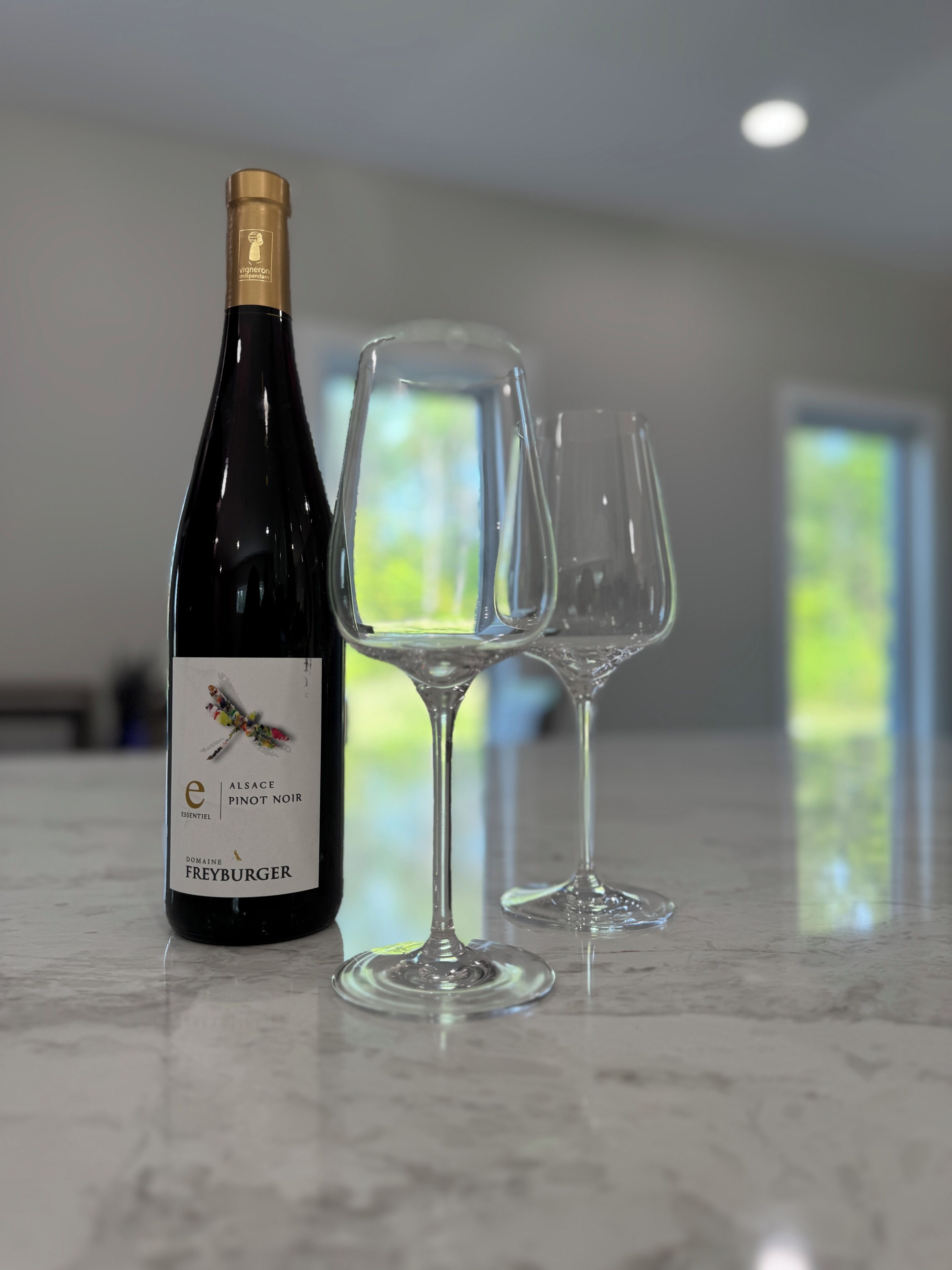 Een fles Alsace Pinot Noir wijn en twee lege wijnglazen op een marmeren aanrecht.