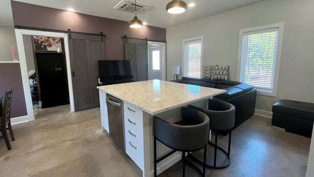 A modern kitchen with a central island, bar stools, a flat-screen TV, and pendant lighting.