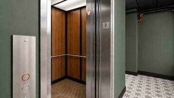 An elevator with a wooden interior, a metallic wall panel, and a floor with a geometric pattern.