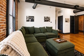 A modern living room with a sectional sofa, a white throw blanket, and a small wooden side table. - Reasonable Doubt --- Vibrant, unforgettable loft in Downtown Port Clinton (Port Clinton)
