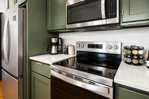 A kitchen with a stainless steel refrigerator, a microwave, a coffee maker, an oven, and a spice rack.