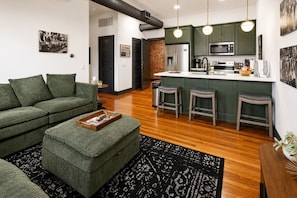 A modern living room with a green sofa, a coffee table, and a kitchen area with green cabinets and a stainless steel refrigerator. - Reasonable Doubt   Vibrant, unforgettable loft in Downtown Port Clinton (Port Clinton)