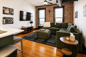 A modern living room with a brick wall, a green sofa, a wooden coffee table, and a television mounted on the wall. - Reasonable Doubt   Vibrant, unforgettable loft in Downtown Port Clinton (Port Clinton)