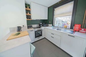 Cocina compacta con armarios blancos, microondas, hervidor de agua y ventana con vistas a edificios.
