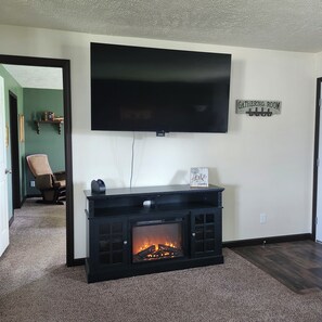 Ein Wohnzimmer mit Kamin, einem flachbildfernseher an der Wand und einem Schild mit der Aufschrift 'GATHERING ROOM'.