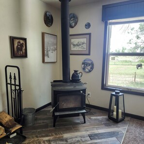A room with a wood-burning stove, framed artwork on the walls, a view of a farm through a window, and a metal gate. - 4 Bedroom, 2 Bath Historical Homestead on the Bighorn River- Longwell Boat Ramp. (Thermopolis)