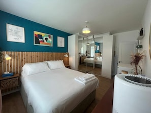 Une chambre d’hôtel avec un lit, une table de chevet, un miroir et des œuvres d’art accrochées aux murs.