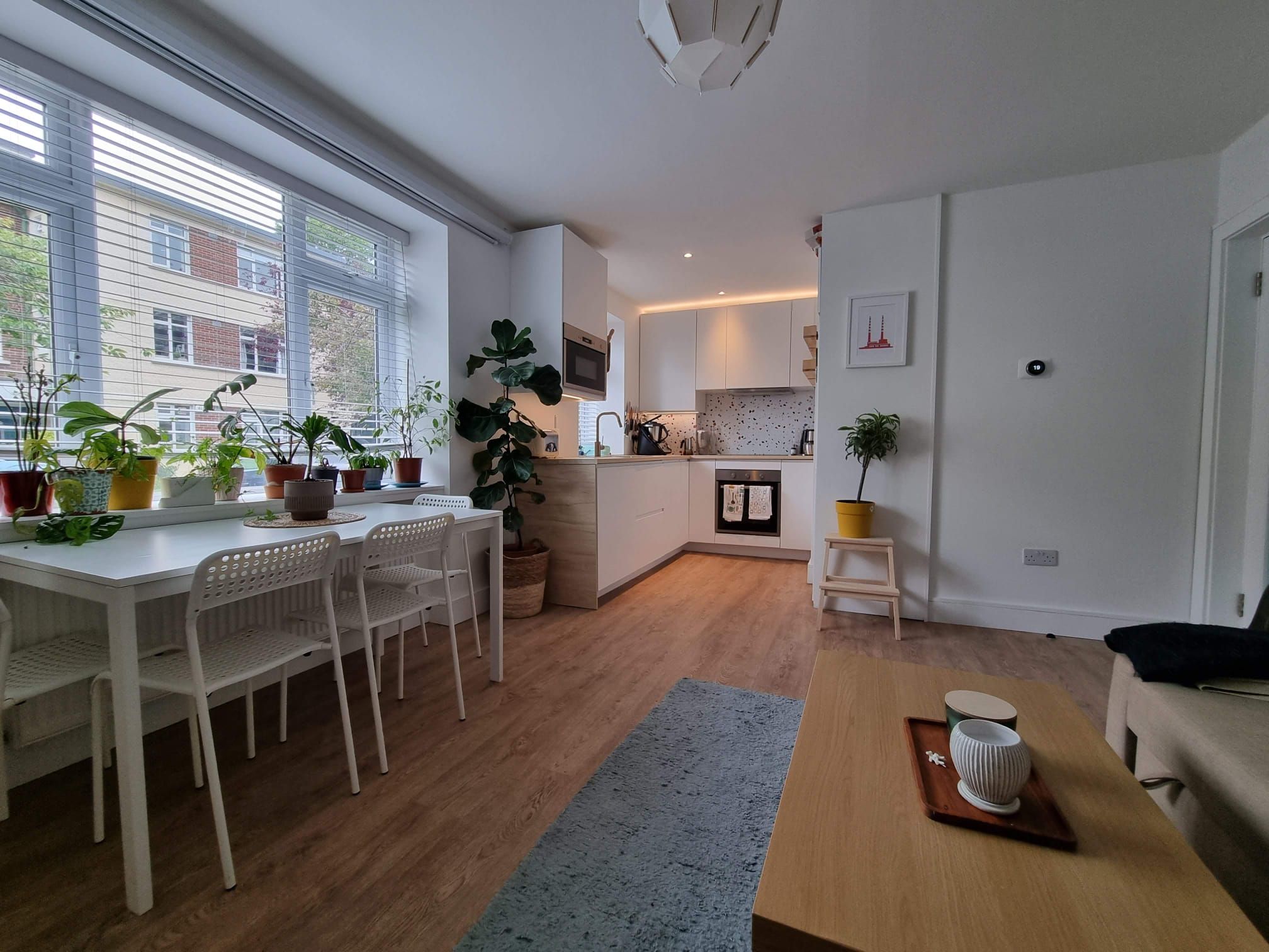 Una cuina moderna amb armaris blancs, una zona de dinar amb taula i cadires blanques, i una petita illa de cuina.