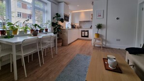 Een moderne keuken met witte kasten, een eethoek met een witte tafel en stoelen, en een klein keukeneiland.