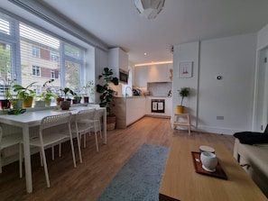 Une cuisine moderne avec des meubles blancs, un coin repas comprenant une table et des chaises blanches, et un petit îlot de cuisine.