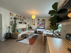 A modern living room with a sofa, coffee table, and a dining area with a table and chairs. There are plants, a guitar, and artwork on the walls. - Charming Sandymount APT Sleeps 4 (Dublin)