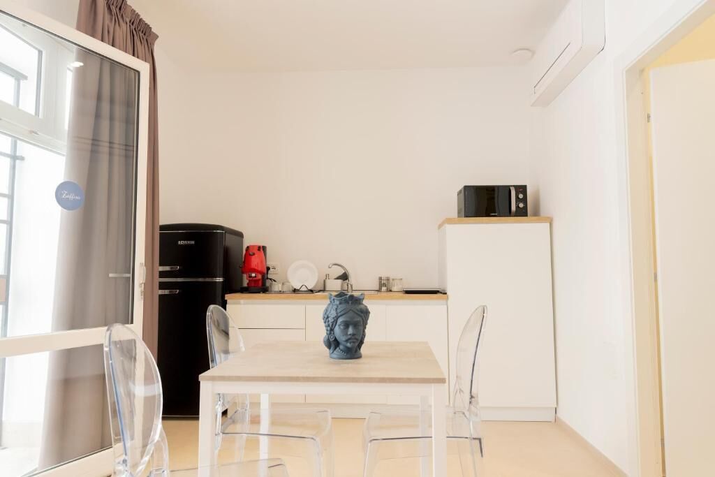 Une cuisine compacte équipée d’un réfrigérateur, d’un four à micro-ondes et d’une machine à café. On y trouve une table à manger avec des chaises et un vase décoratif.