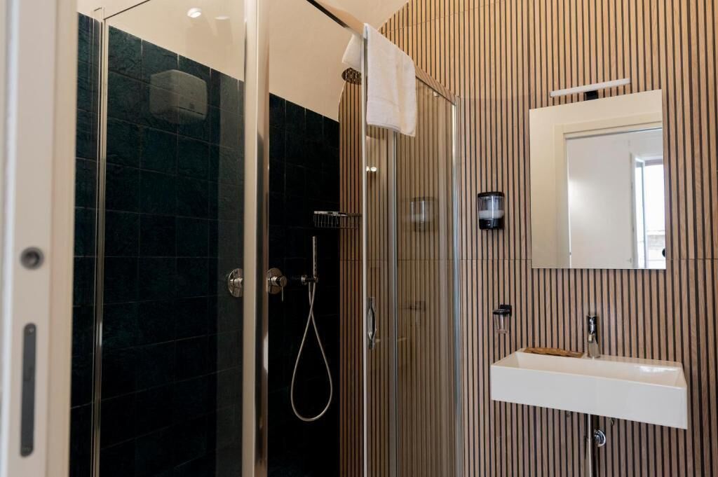 Ein modernes Badezimmer mit einer gläsernen Duschkabine, einem weißen Waschbecken und einem Spiegel an der Wand.